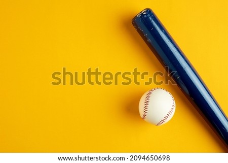 Blue wooden baseball bat and a baseball ball on yellow background with copy space.
