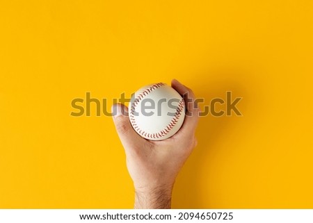 Male hand holds a baseball ball on yellow background. Top view.