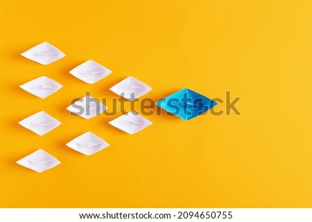 Leadership, collaboration, cooperation or partnership in business concept. Blue paper boat leads white paper ships on yellow background.  Royalty-Free Stock Photo #2094650755