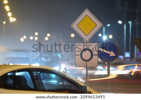 Roundabout road signs with blurred cars on city street traffic at night. Urban transportation concept