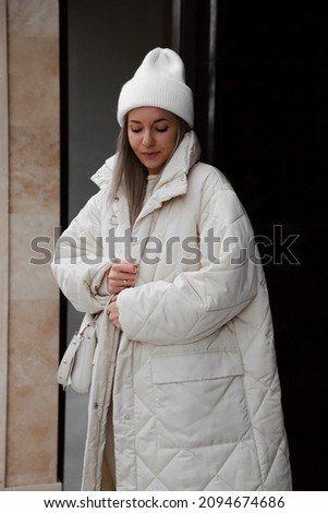 portrait of beautiful blonde girl dressed in white quilted down jacket, white pants and sweater, knitted hat, stylish trendy fashion outlook, lifestyle model, winter milky cozy outfit Royalty-Free Stock Photo #2094674686