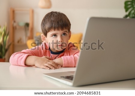 Little boy watching cartoons on laptop at table in living room