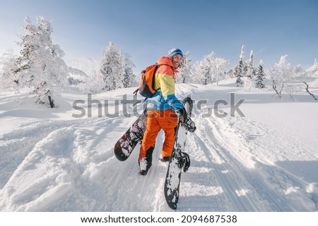 Snowboarder walking with a snowboard in the winter forest. Ski touring in the snowy mountains on a sunny day Royalty-Free Stock Photo #2094687538