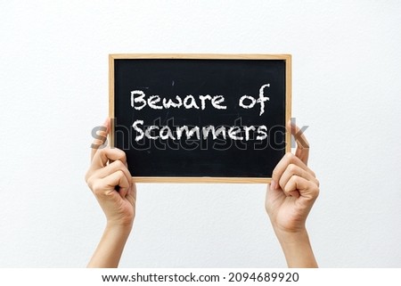 Cropped hands holding a chalkboard with "Beware of Scammers" against a white background Royalty-Free Stock Photo #2094689920