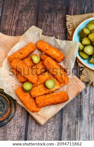 Close up of   Crispy breaded  deep fried fish fingers with breadcrumbs served  with remoulade sauce,pickled cucumbers and   lemon Cod Fish Nuggets on rustic wood table background