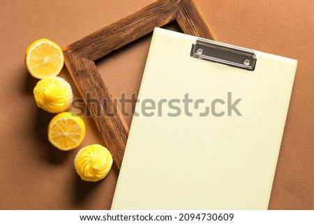Composition with clipboard, picture frame, lemons and cupcakes on color background