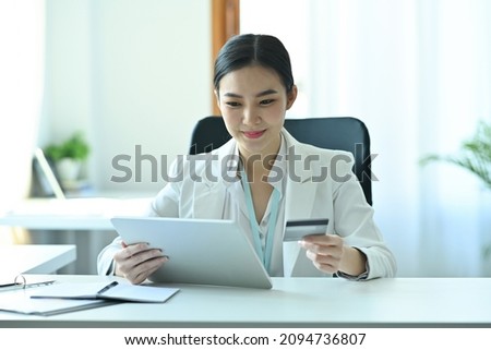 Photo of a confident businesswoman holding a credit card and digital tablet at the modern working desk.
