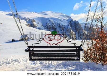 Swing between two trees. 
Background mountain peaks covered with snow