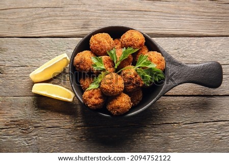 Frying pan with tasty cod cutlets and lemon on wooden background Royalty-Free Stock Photo #2094752122