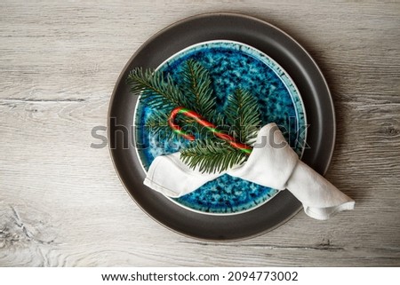 Christmas dinner. Festive table setting, two plates with Christmas decor. Gray and blue plate, white napkin and spruce branches with candy.