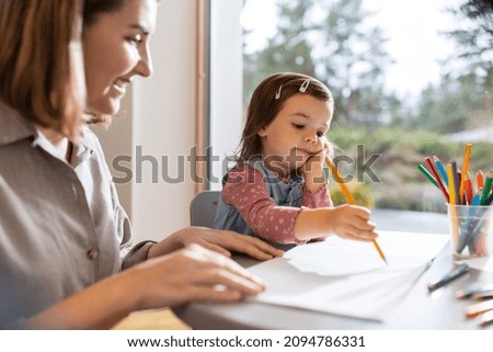 family, motherhood and leisure concept - mother spending time with her little daughter and drawing at home