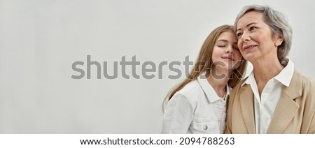 Happy caucasian granddaughter and her senior grandmother on white background in studio. Age and generation concept. Idea of family relationship and closeness. Blonde girl with closed eyes. Copy space