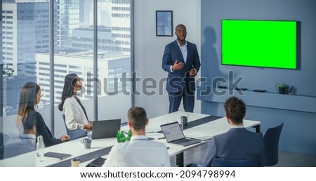 Diverse Office Conference Room Meeting: Successful Black Male Project Manager Uses Green Screen Chroma Key Wall TV Presenting Product to Group of Investors. e-Commerce Strategy. Wide Static Shot