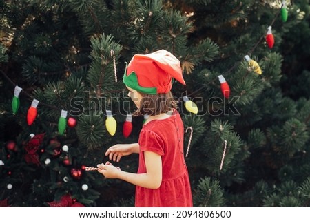 Child waiting for Christmas in wood in summer. portrait of little girl in red dress decorating christmas tree. winter holidays and people concept. Merry Christmas and Happy Holidays
