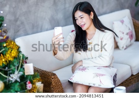 Portrait Cute beautiful positive smile young asian woman using smartphone video call or Selfie at home in the living room indoors Decoration During Christmas x-mas and New Year holidays.