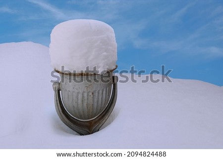 An old cast-iron urn filled with snow, against a snowdrift and the sky.