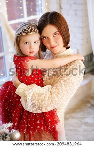 Mom and daughter in beautiful festive dresses hug and smile against the background of New Year's garlands and festive decorations. Merry Christmas! family, winter holidays concept