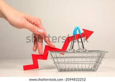 The fingers of a woman's hand step up the arrow of a chart lying on a shopping basket. Crisis and rising commodity prices concept Royalty-Free Stock Photo #2094832252