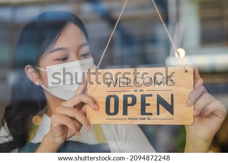 Reopen, asian young owner retail, coffee shop woman turning sign board open wearing face mask, protect to pandemic of coronavirus, reopen store after close lockdown quarantine in covid-19, new normal.