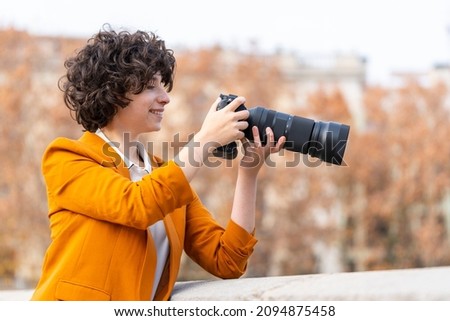 Young brunette woman with curly hair taking a picture with telephoto lens