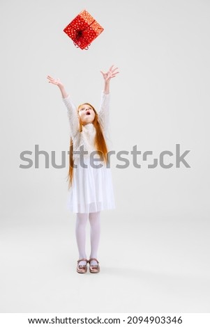 Merry Christmas, birthday, holiday event. Happy and delightful child, girl holding big present box over white background. Concept of childhood, family, happiness, emotions, facial expression, ad