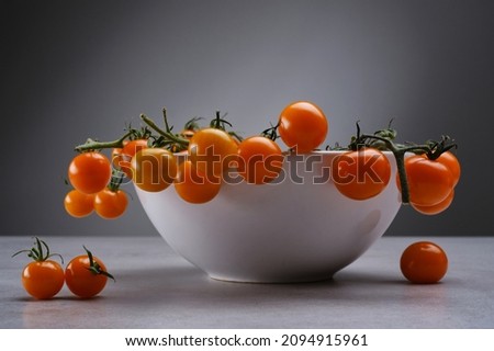 Yellow cherry tomatoes in a white porcelain bowl on the gray granite table. Sprig of cherry tomatoes on a gray concrete background. Selective focus