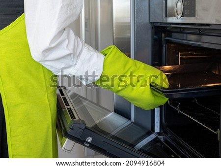close-up view of a person wearing green gloves placing a metal tray into the oven, horizontal picture