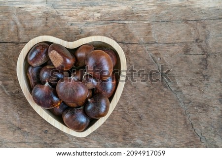 chestnuts, ripe and raw chestnut fruits in a heart shaped bowl on wooden table or background or surface with copy space.