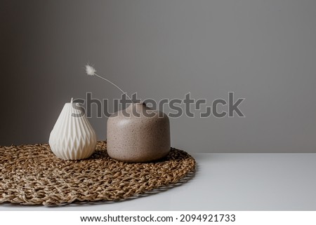 Cozy home interior decor, aromatic burning candles in glass glowingon with natural oil, selective focus of fluffy bunny tail grass, brown jar, lotus flower candle, round matt ceramic