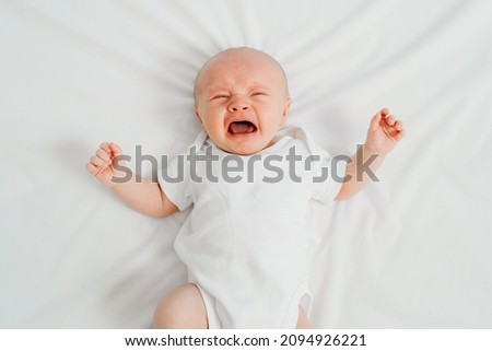 a newborn baby cries on a white sheet. childish tantrums. colic and abdominal pain in infants. medicines and vitamins for babies. top view. Royalty-Free Stock Photo #2094926221