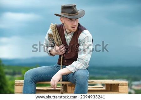 Portrait of farmer or cowboy outdoor. Cowboy with lasso rope on sky background.