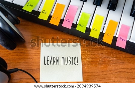 Sticky note with the words -Learn Music!-, Next to a piano and headphones. Learning music concept.