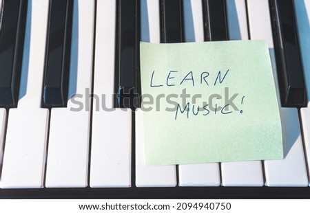 A sticky note with the words -Learn music!- on the keyboard of a piano. Learning music concept.