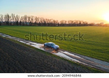 Aerial view of sedan car driving fast on dirt road at sunset. Traveling by vehicle concept. Royalty-Free Stock Photo #2094946846