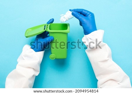 Throwing away a medical mask in a green container for recycling on a blue background. Blue face masks after use. The use of medical masks.