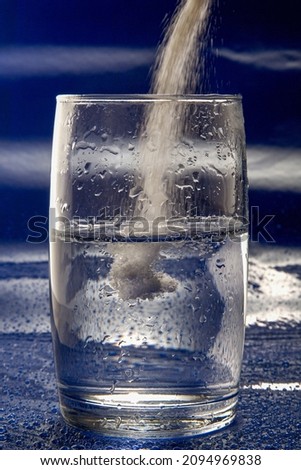 A vertical shot of medicine in powder forms into a water glass