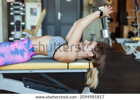Young woman with perfect body trains with a dumbbell while lying on a bench. Strong body, bodybuilding and fitness Royalty-Free Stock Photo #2094981817