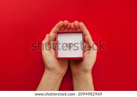 a ring with a large stone in a box in the hands of a child on a red background Royalty-Free Stock Photo #2094982969