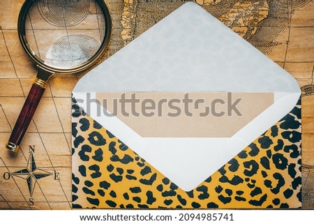 Envelope with a jaguar skin color pattern, and a stylish magnifying glass on the background of an old yellowed map, Creative layout, Beautiful adventure, wildness and discovery concept, Flat lay 