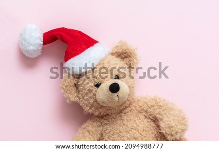 Christmas present. Teddy bear wearing Santa hat on pink color background, Kids holidays gifts, toys and stuffed animals. Holiday greeting card.