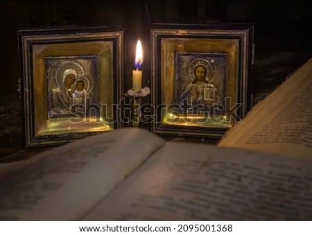 Icons of the Virgin Mary with the infant Christ and Nicholas the saint at a burning candle illuminating the opened sacred religious books
