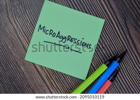 Microaggressions write on sticky notes isolated on Wooden Table.