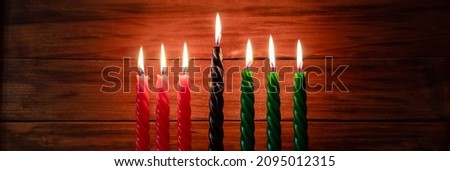 Celebration of African American Kwanzaa festival. Seven burning candles red, black and green in traditional Kinara candlestick. Symbols of African heritage on wooden background. Banner format