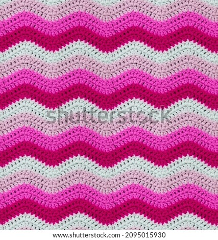 Seamless knitted pattern in the form of zigzags is crocheted with multi-colored threads. Acrylic baby yarn. Contrasting pink range of shades.