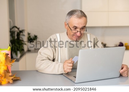 Happiness of wellness elderly asian man with white hairs sitting on sofa using computer laptop and using credit card to shopping online and payment at home,Senior lifestyle at home concept.