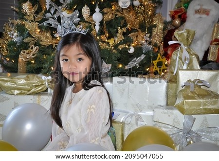 Beautiful little girl sitting in front of Christmas tree with lots of gifts