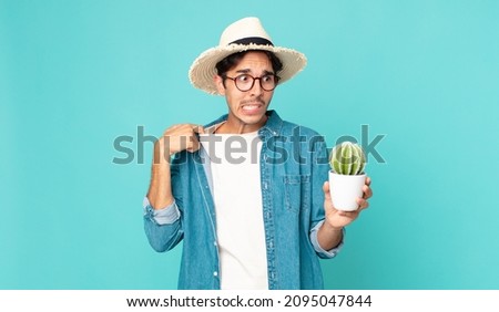 young hispanic man feeling stressed, anxious, tired and frustrated and holding a cactus