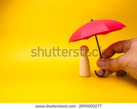 Hand holding red umbrella with peg doll on a yellow background.Insurance cover concept. Royalty-Free Stock Photo #2095050277