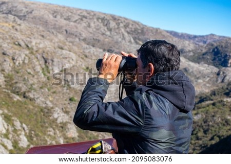 middle-aged man as an adult looking through binoculars while trekking