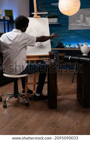 Man painter sitting in front of canvas drawing vase making shadows with graphic pencil working at creative project during art lesson. Student artist painting usinf professional draw tools